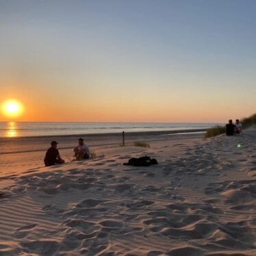 Een groep mensen die bij zonsondergang op het strand zitten.